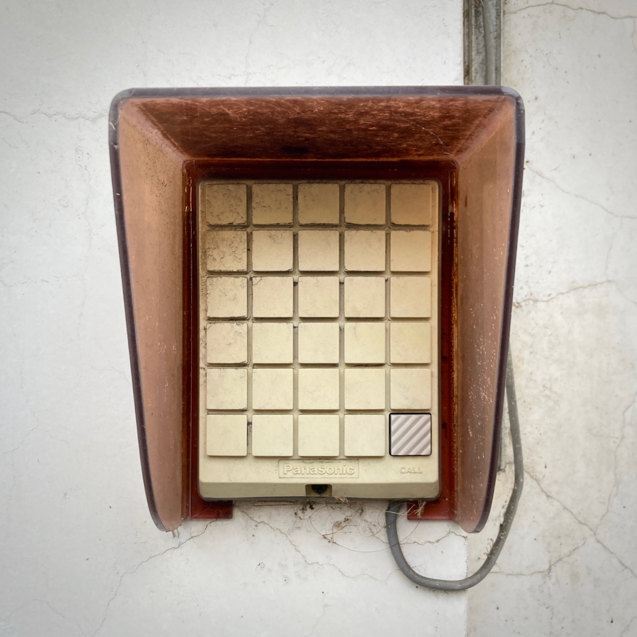 A photograph of a beige control panel, attached to a wall. There's a grid of 5 × 6 buttons – except they're not buttons, they're just a mold where the buttons would be. Only the lower left of these 30 potential buttons is actually a button, and it's very lightly embossed with the word 'CALL'.